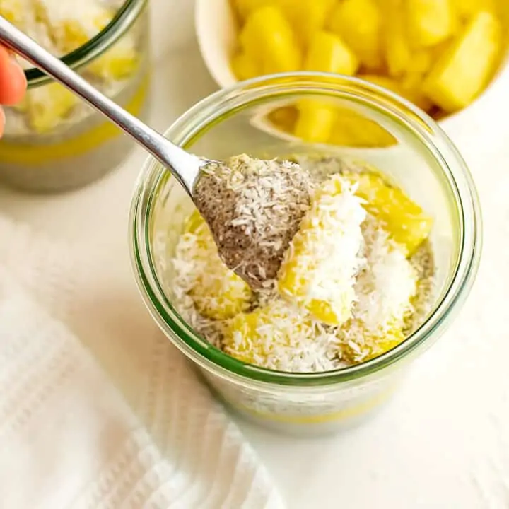 Pineapple mango chia pudding with a spoonful of pudding on being lifted out of the glass.