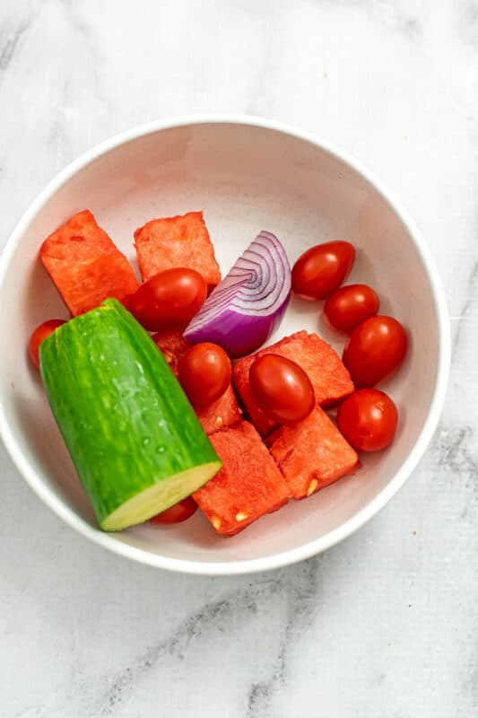 Cucumber, watermelon cubes, tomatoes and red onion in a bowl.