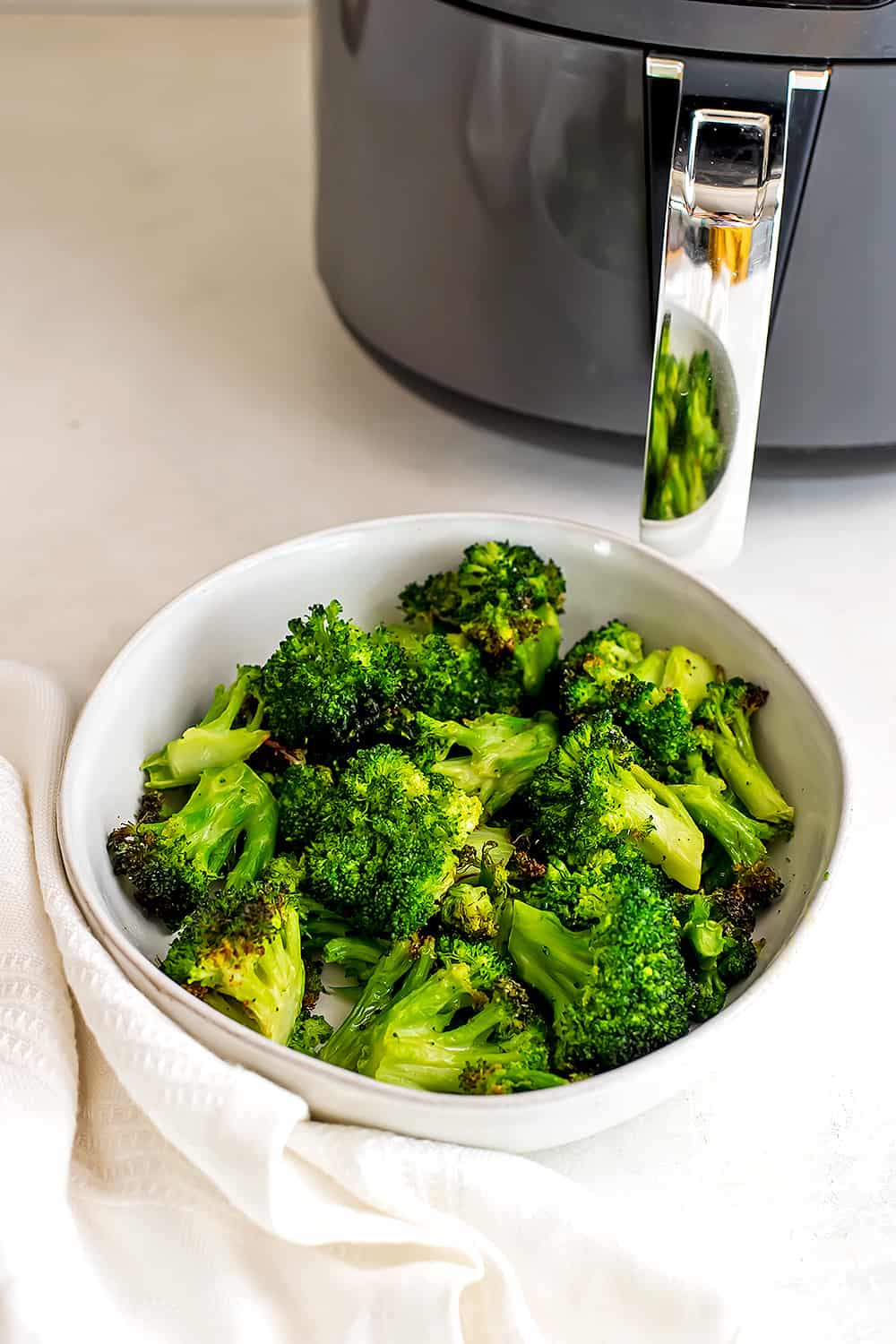 Broccoli in a white bowl in front of the air fryer.