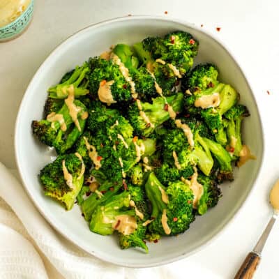 Broccoli in a white bowl with chili flakes and tahini drizzled.