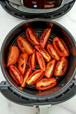 Roma tomatoes cut into quarters lined in air fryer basket.