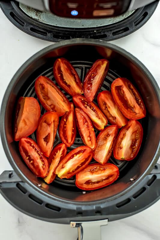 Roma tomatoes cut into quarters lined in air fryer basket.
