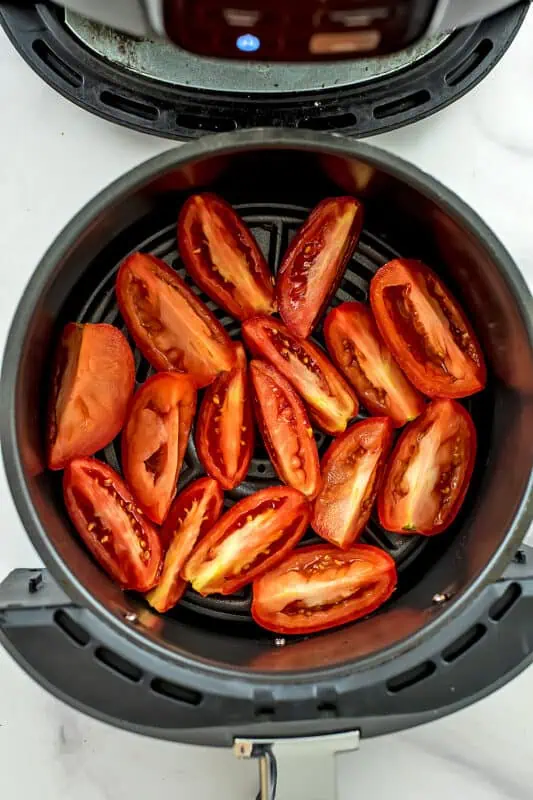 Roma tomatoes cut into quarters lined in air fryer basket.