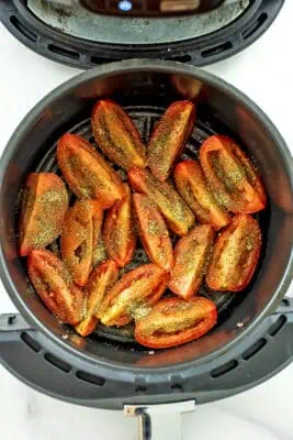 Spices over roma tomatoes in air fryer basket.