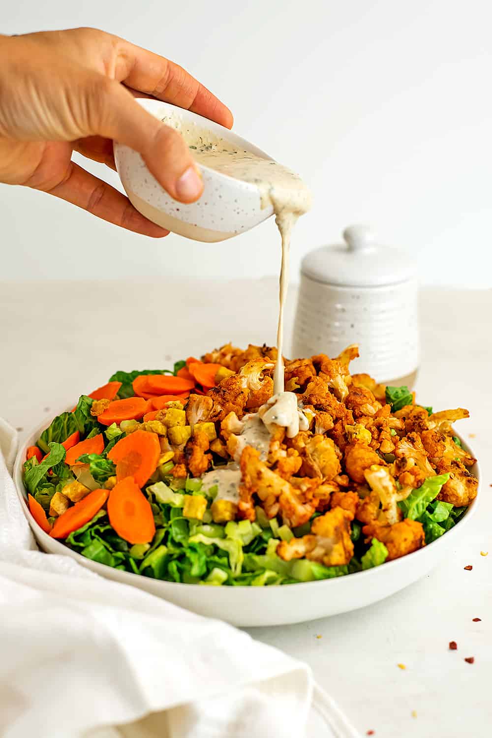 Tahini ranch dressing being poured over buffalo cauliflower salad.
