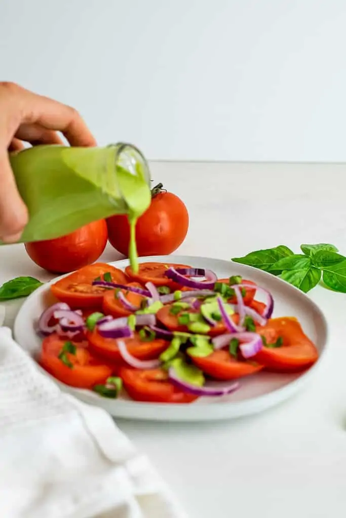 Creamy basil dressing being poured over a tomato salad.