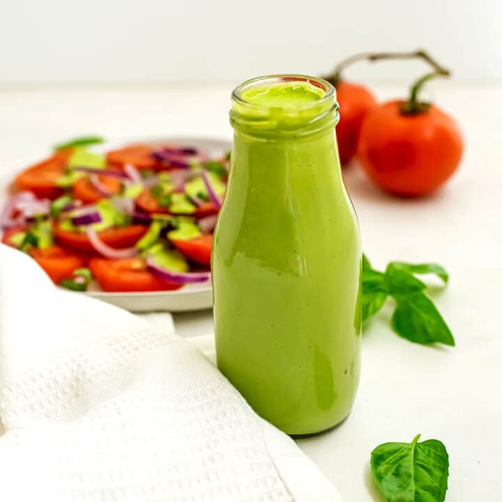 Bottle of creamy basil dressing in front of a plate of tomatoes.