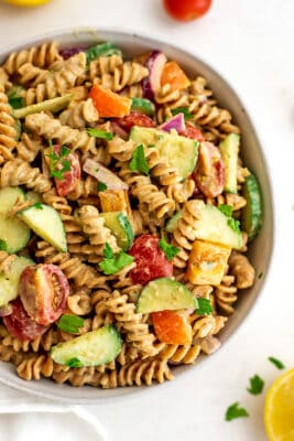 Hummus pasta salad in large bowl with lemons around the bowl.
