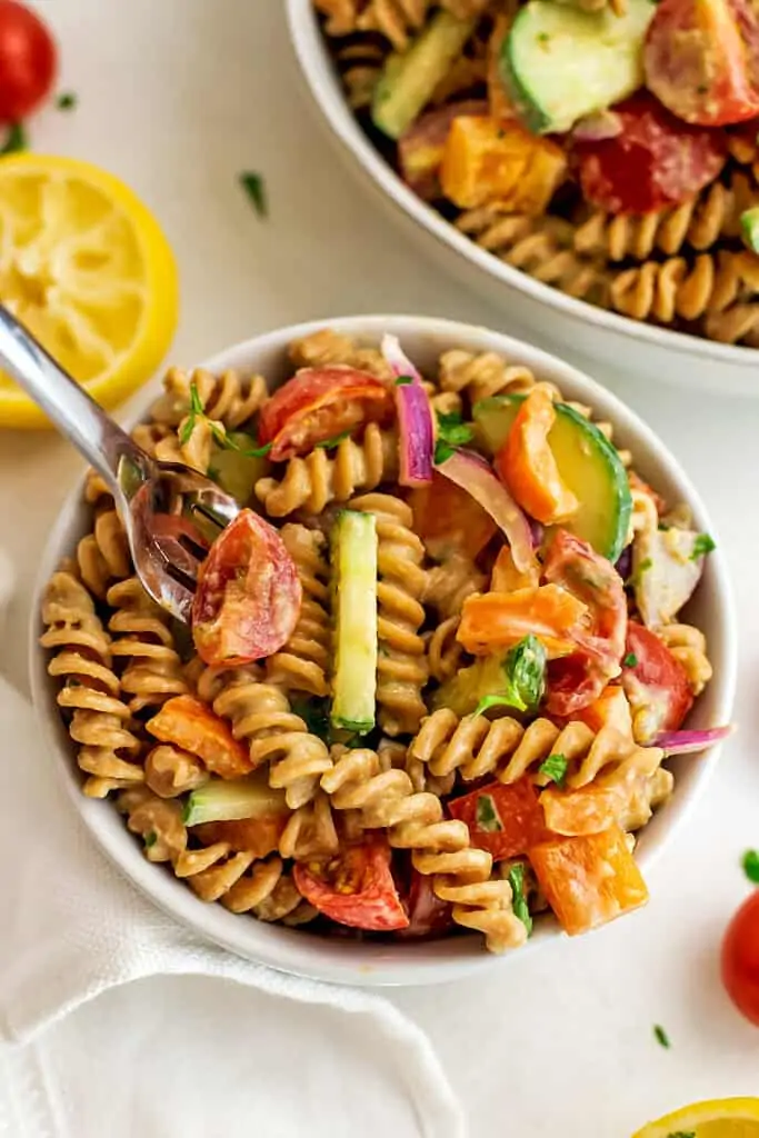 Fork in a bowl of vegan hummus pasta salad.