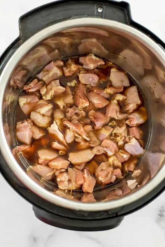 Cubed chicken thighs added to rice mixture in instant pot.
