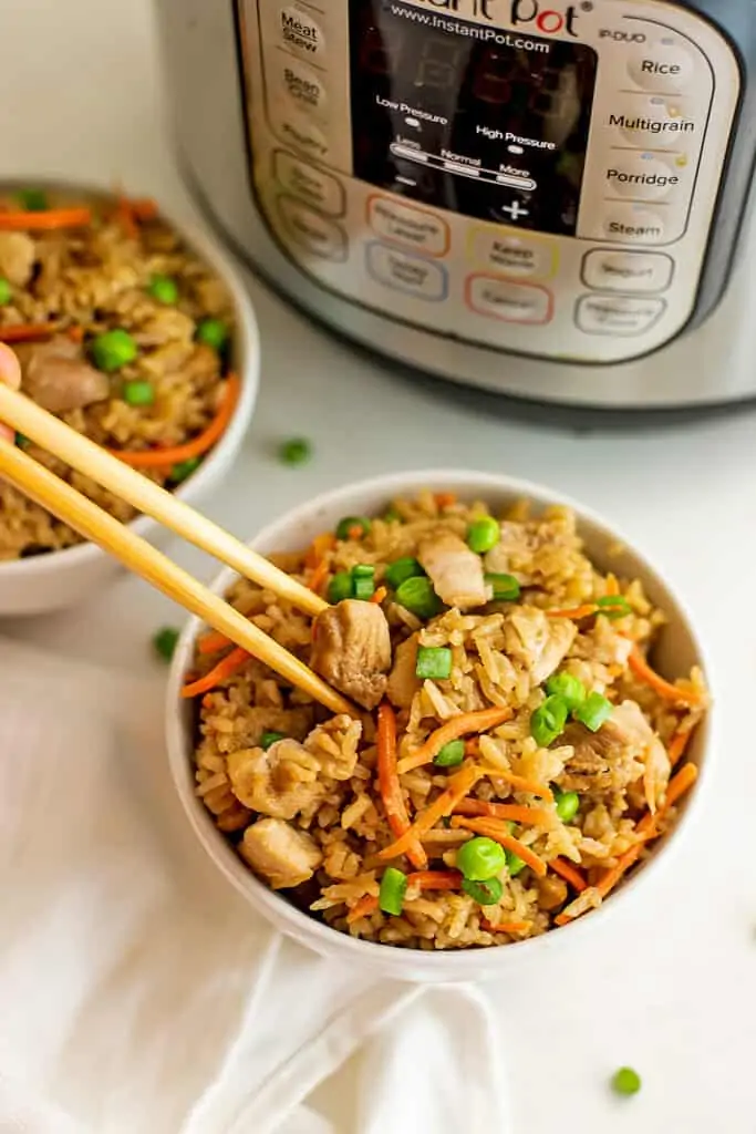 Chopsticks getting a serving of chicken fried rice in front of instant pot.