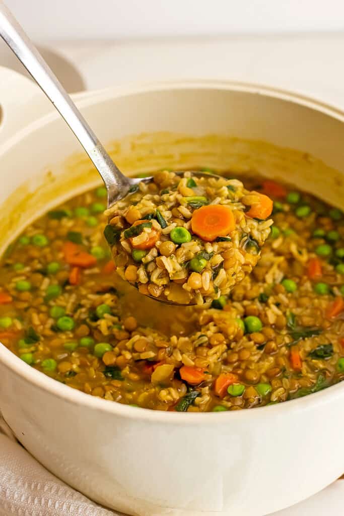 Ladle full of soup over a white pot.