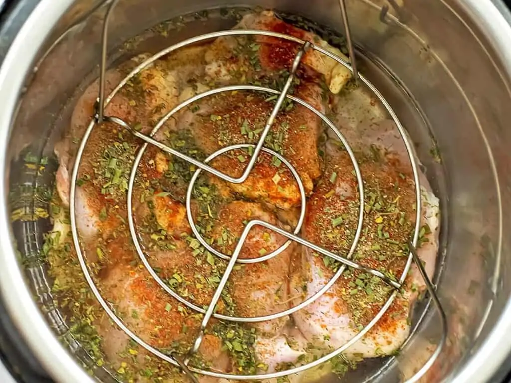 Chicken thighs with seasoning and a trivet over top.