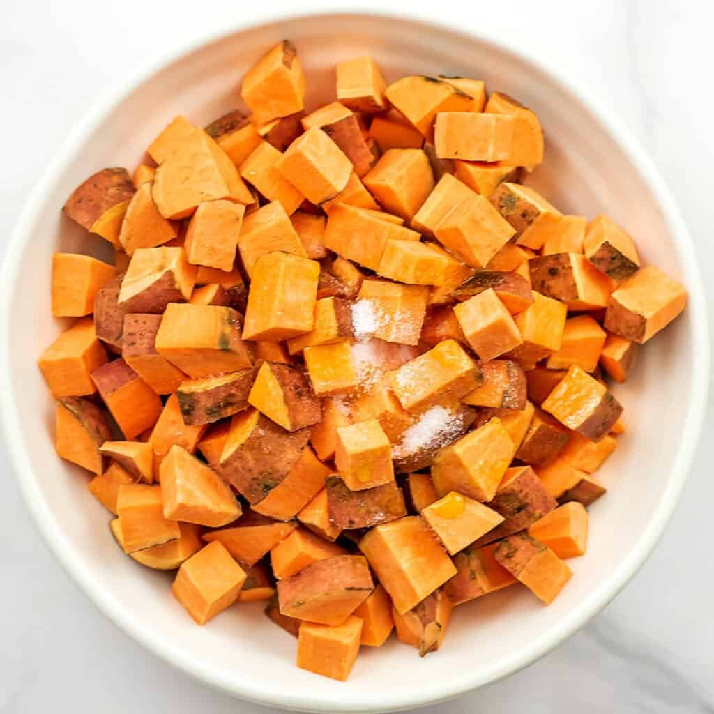 Cubes of sweet potatos in white bowl with seasoning on top.