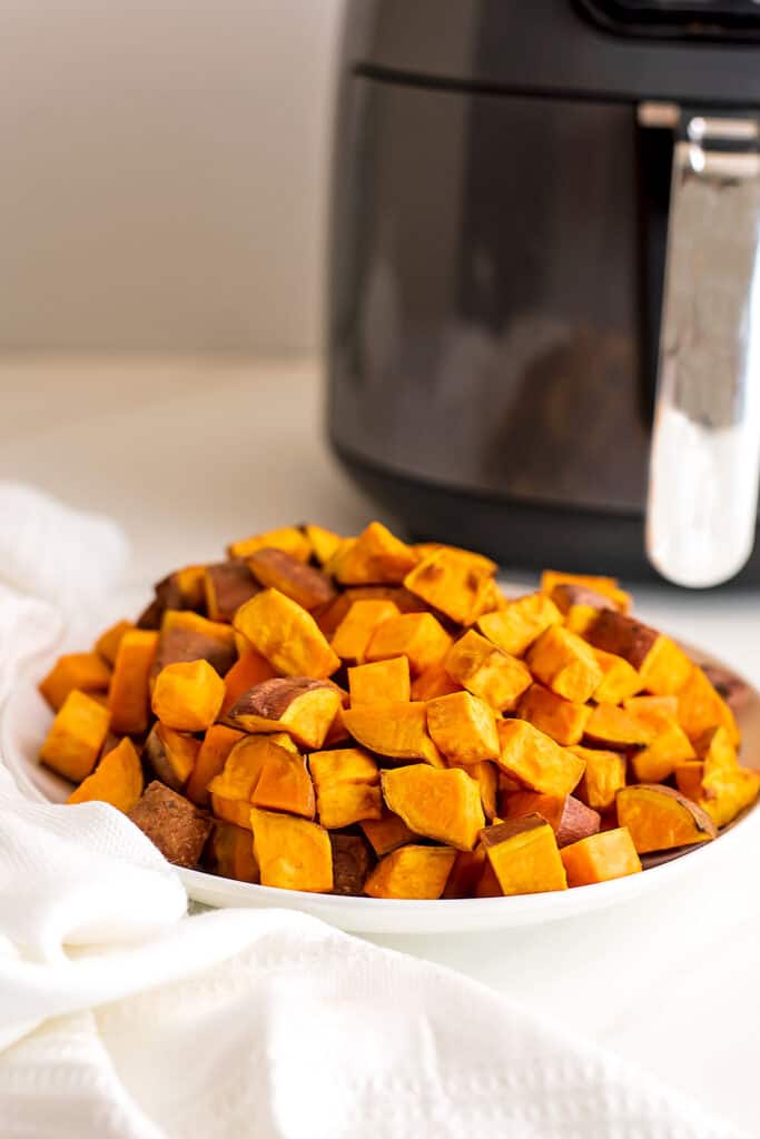 Sweet potato cubes in white bowl, air fryer in background.