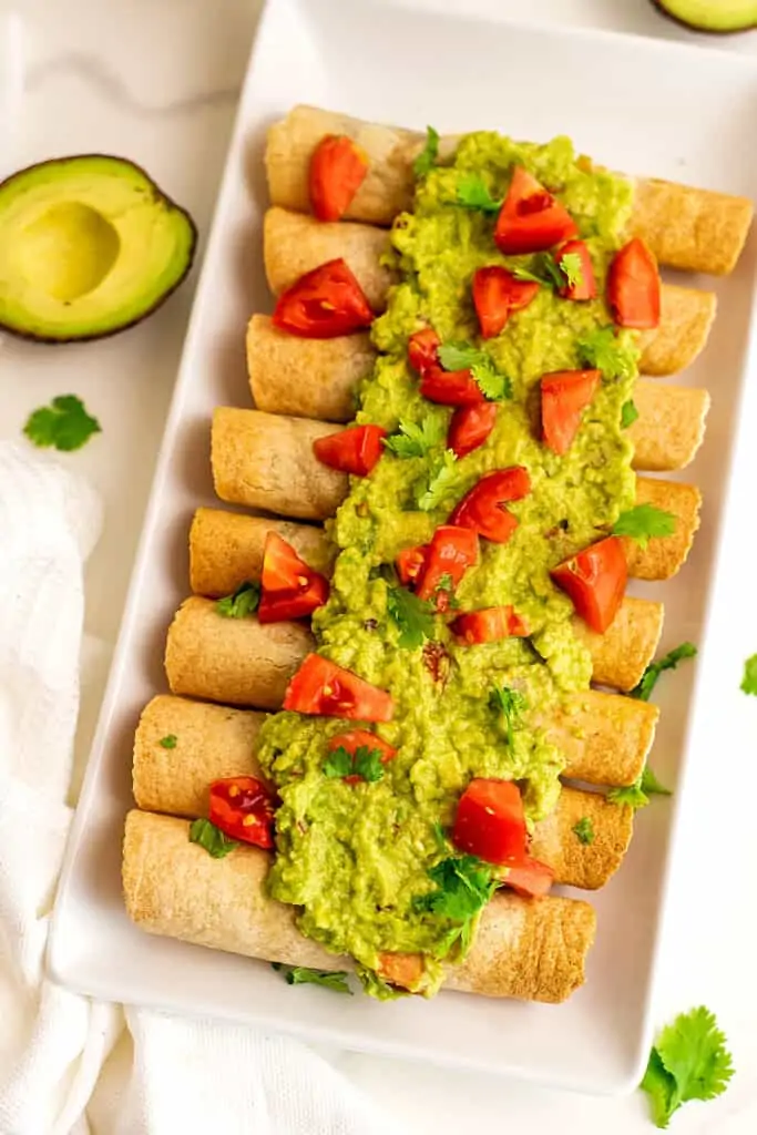 Vegan taquitos topped with guacamole and tomatoes.