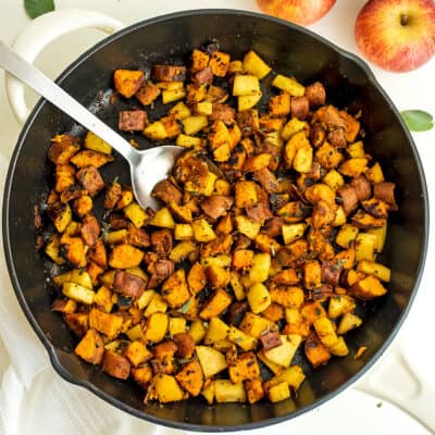 Cast iron skillet filled with apple sweet potato hash, spoon in skillet.