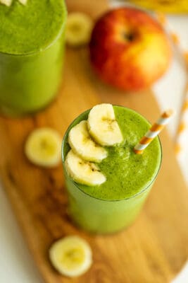Banana apple spinach smoothie with orange striped straw in cup.