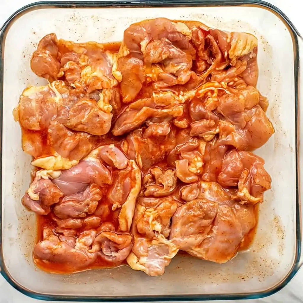 Chicken thighs flipped over with buffalo sauce on top before baking.