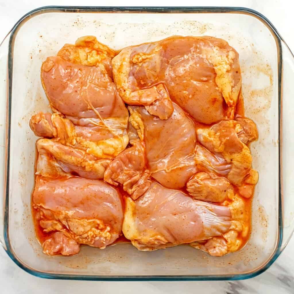 Buffalo chicken thighs in glass casserole dish before baking.
