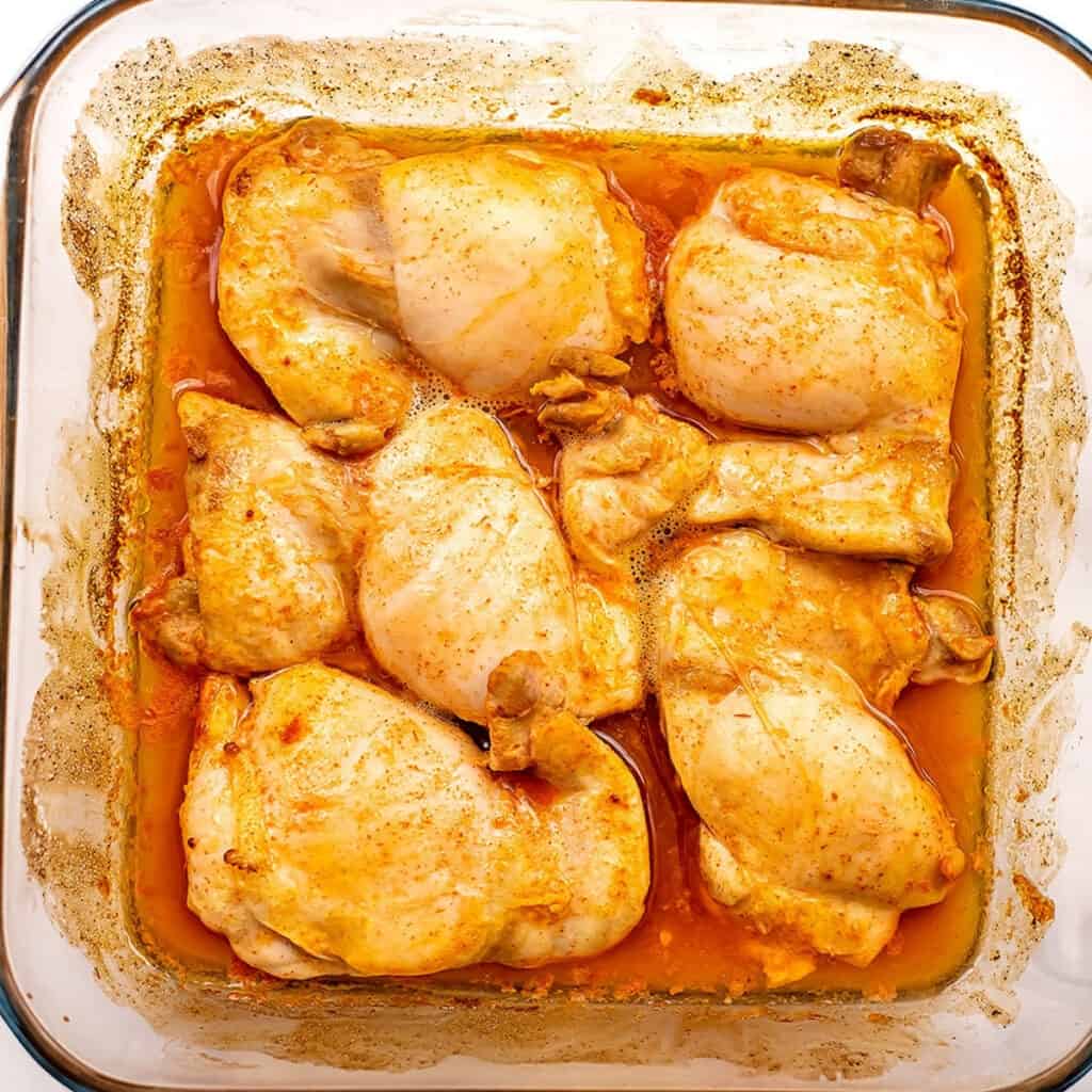 Chicken thighs in buffalo sauce in glass casserole dish.