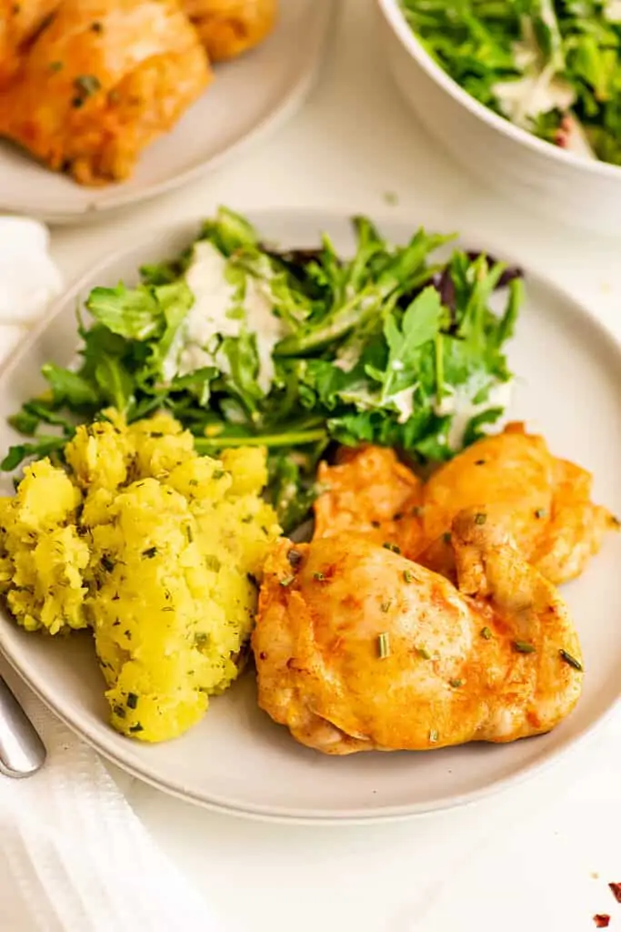 Spicy chicken thighs on a plate with salad and mashed yellow potatoes. 