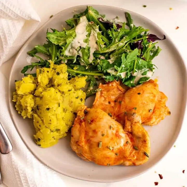 Buffalo chicken thighs, yellow potatoes and salad on plate.