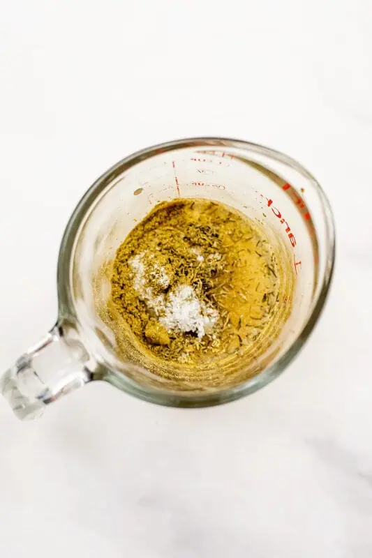 Glass measuring cup filled with tahini, apple cider vinegar and spices.