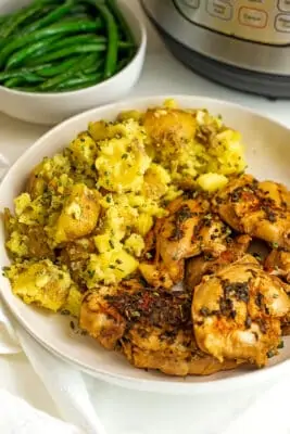 Chicken thighs and potatoes in a large white serving dish.