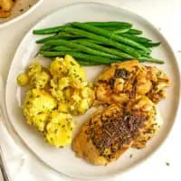Chicken thighs, smashed potatoes and green beans on a white plate.
