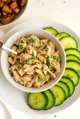 Tuna salad in a bowl with spoon in bowl and cucumbers on plate.
