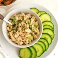 Low FODMAP tuna salad in white bowl on plate with sliced cucumbers.