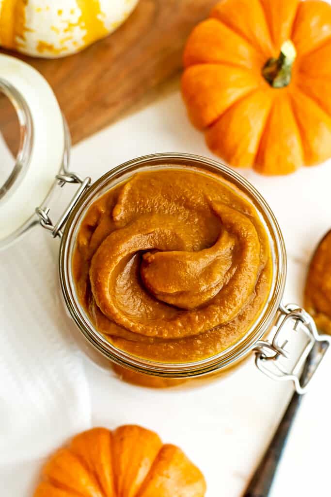 Maple pumpkin butter in jar with pumpkins in background. 