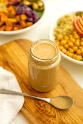 Maple tahini dressing in glass jar on wooden platter.