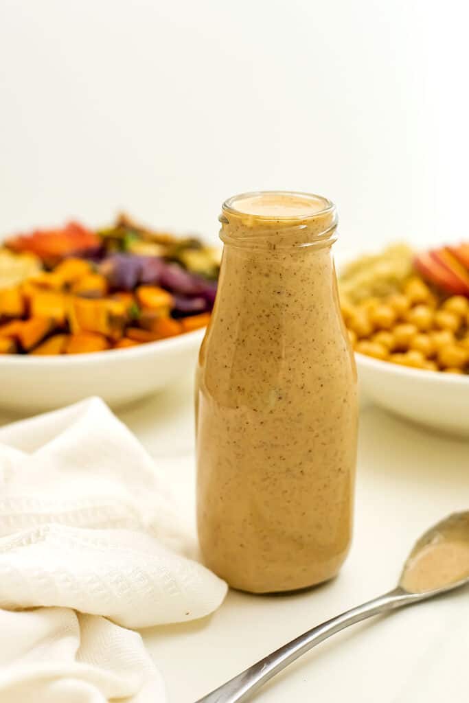 Maple tahini dressing in a bottle in front of salad bowls.