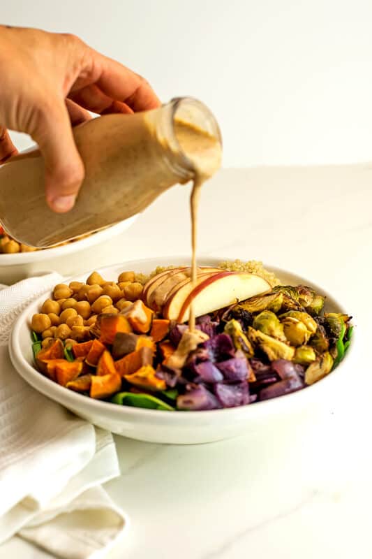 Mustard tahini dressing being poured over salad.