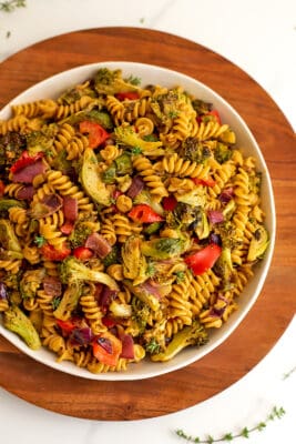Bowl filled with roasted veggie pasta salad on wooden plate.
