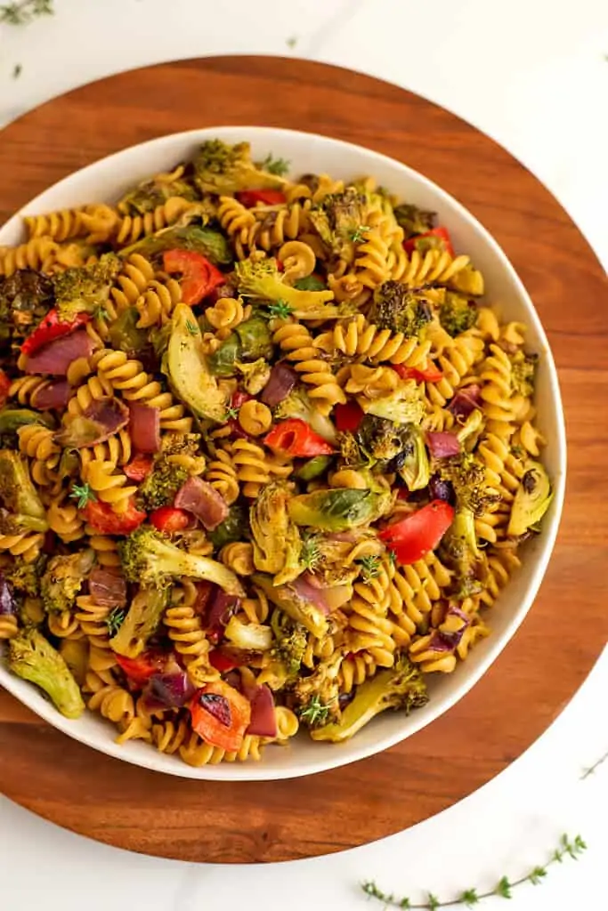 Bowl filled with roasted veggie pasta salad on wooden plate.
