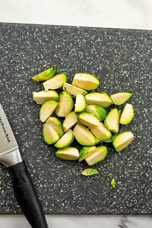 Brussel sprouts cut into quarters on a grey cutting board.
