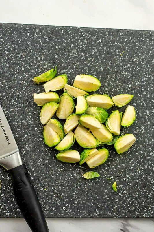 Brussel sprouts cut into quarters on a grey cutting board.