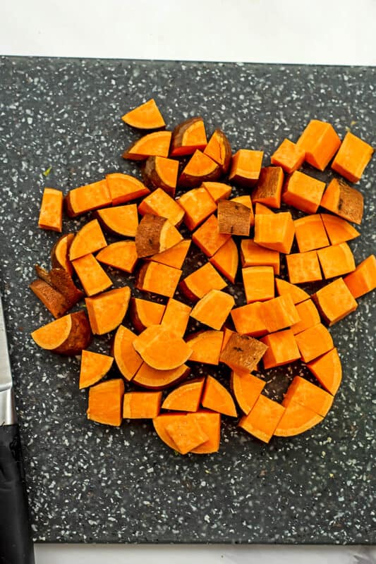 Sweet potato cut into cubes on a grey cutting board.