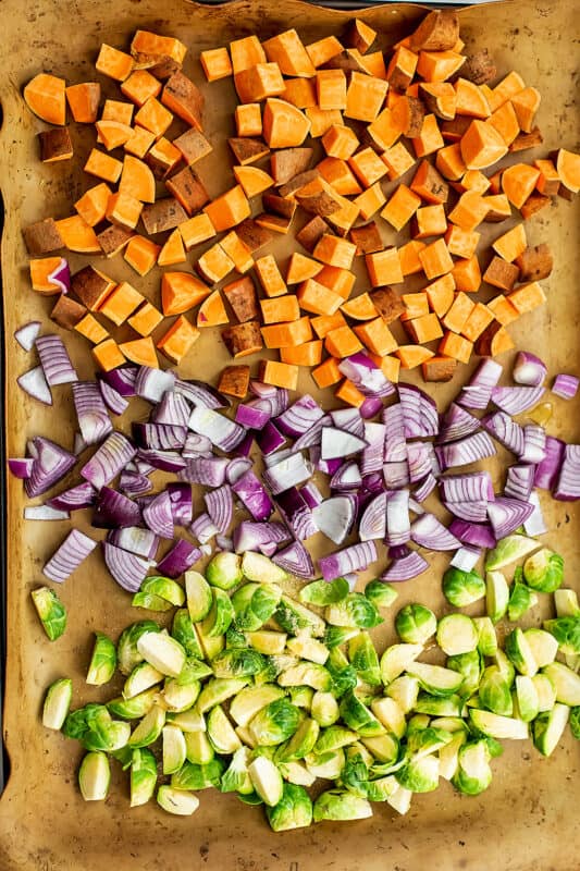 Sweet potatoes, red onion and brussel sprouts on a sheet pan before cooking.
