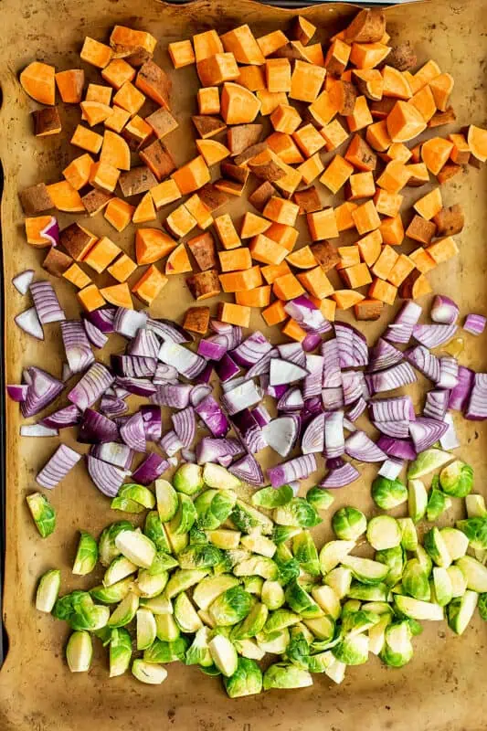 Sweet potatoes, red onion and brussel sprouts on a sheet pan before cooking.
