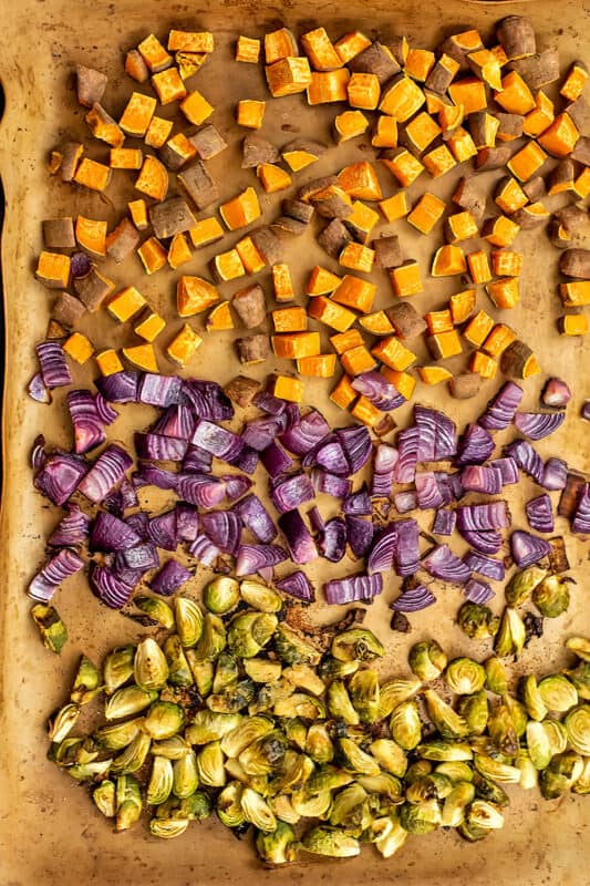 Sweet potatoes, red onion and brussel sprouts on a sheet pan after cooking.