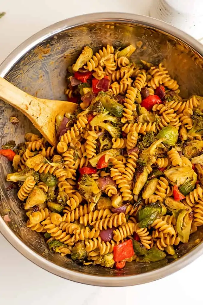 Pasta salad with roasted vegetables in silver bowl after stirring.