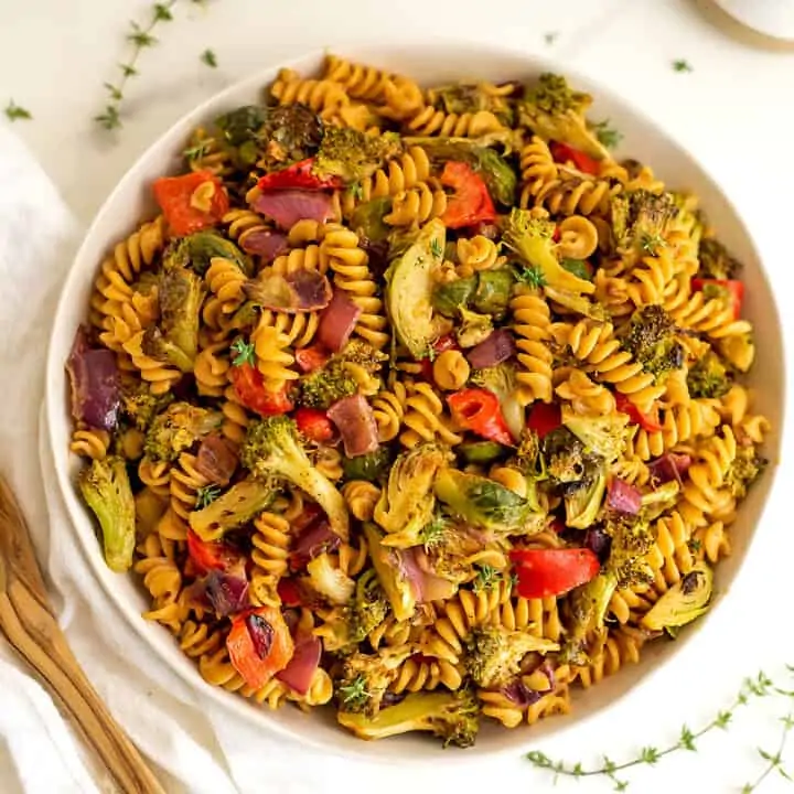 Roasted veggie pasta salad in white bowl with spoon on side.