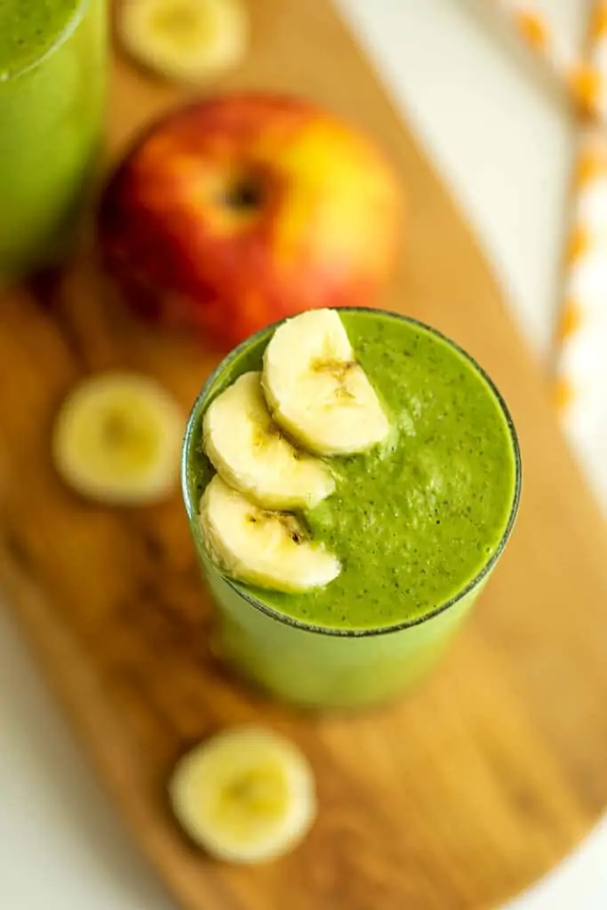 Spinach apple banana smoothie on a wooden trivet.
