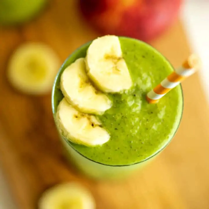 Apple banana spinach smoothie in glass with straw and banana on top.