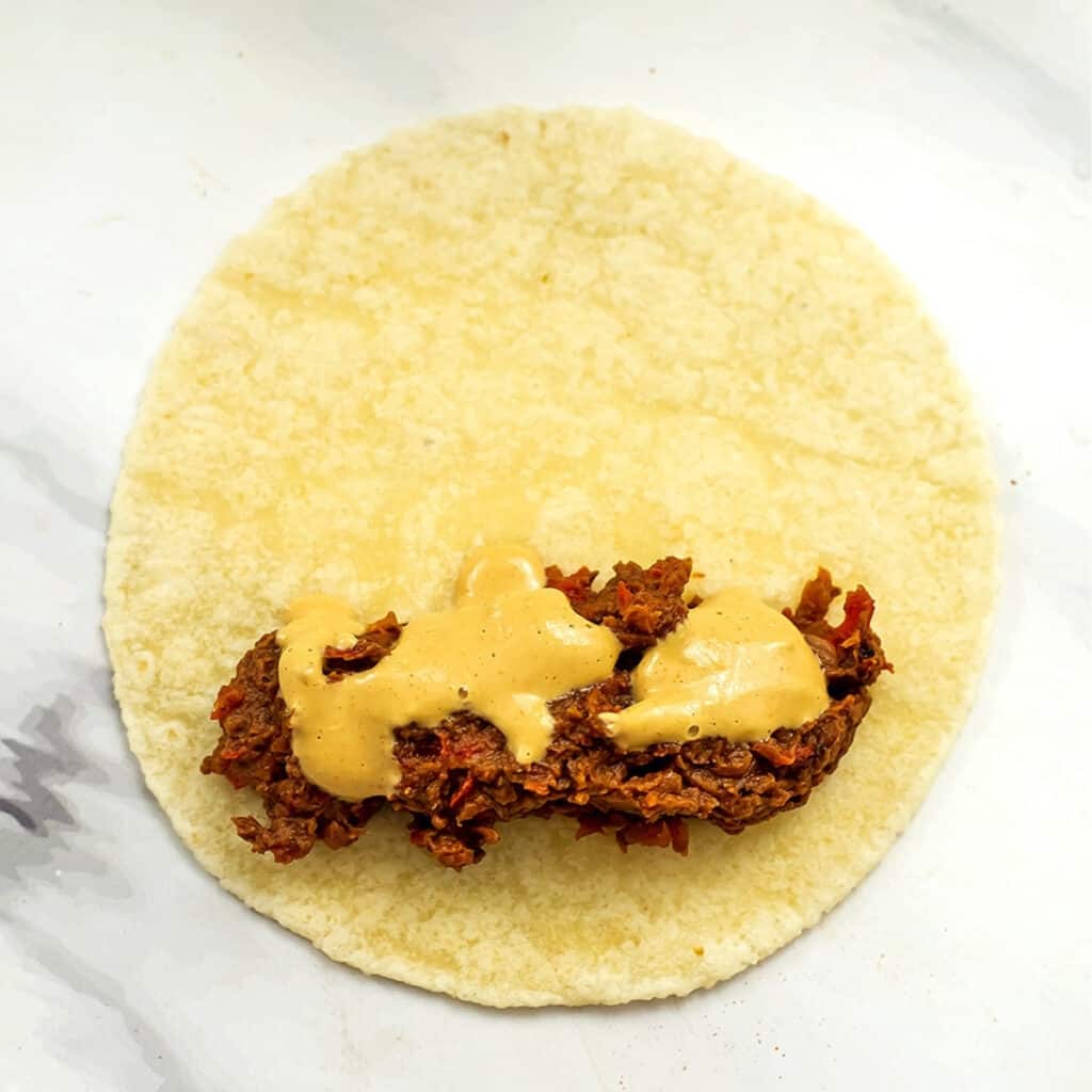 Black bean filling with vegan nacho cheese on tortilla.