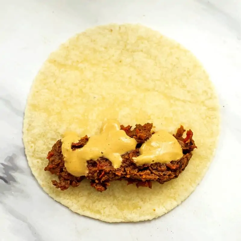 Black bean filling with vegan nacho cheese on tortilla.